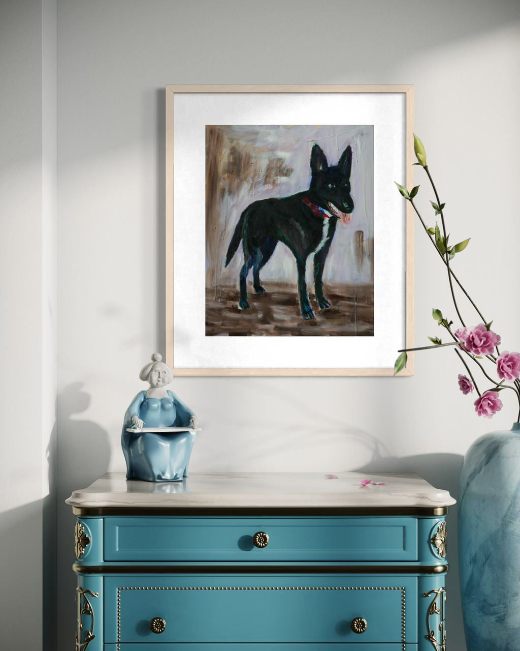A framed art print of a black dog with a red collar, displayed on a light gray wall above a teal blue dresser with a marble top. A blue figurine and a vase with pink flowers are placed on the dresser.